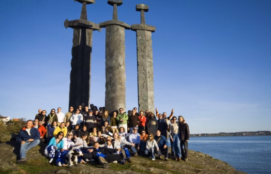 Grupo posando ante un monumento de tres columnas de piedra junto al agua