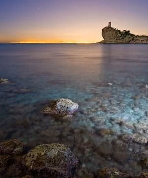Cala rocosa al atardecer con una silueta de castillo