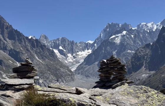 Dos mojones de piedras apiladas en primer plano con el glaciar Mer de Glace y picos nevados al fondo