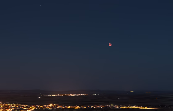 Luna en tonos rojizos durante un eclipse, sobre las luces de un pueblo de noche