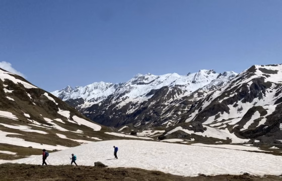 Una familia caminando sobre un nevero en un valle del Pirineo, con picos nevados alrededor